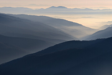 mountain ranges and slopes covered with forest in fog