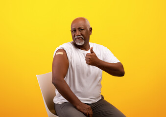 Vaccinated senior black guy with adhesive plaster bandage after coronavirus antiviral vaccine injection showing thumb up - obrazy, fototapety, plakaty