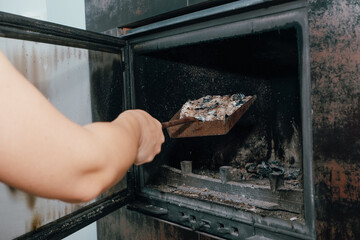Fireplace cleaning. A woman's hand holds a shovel with ash in a burnt-out fireplace. Close up view.