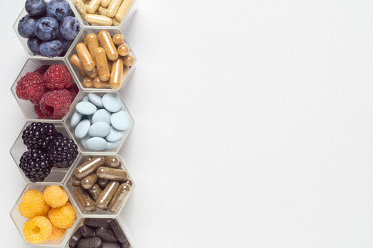 Fresh berries, pills and capsules in honeycomb like hexagonal jars