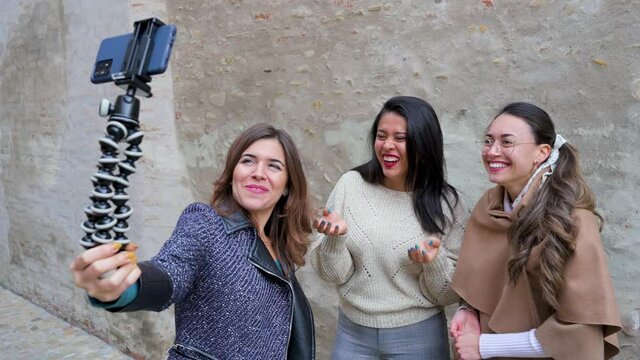 Three young attractive females holding a smartphone and talking ato camera with smiley excited faces.