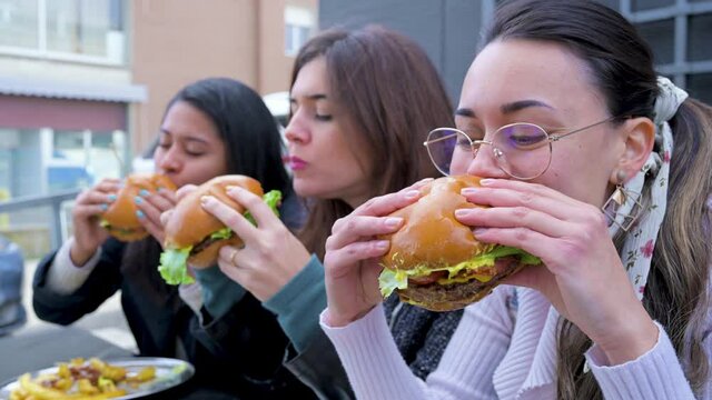 Side view close-up Young females friends eating and biting hamburgers.