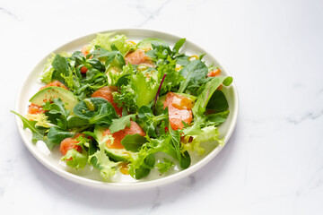 Salmon, avocado and assorted lettuce salad on white marble background