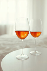 Two glasses of wine are on a white table in front of the window