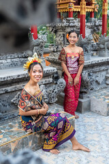 Portrait of two young balinese girls with traditional costume with offering in bali temple, indonesia