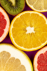 Ripe slices of colorful fruits. Lemon, oroblanco, kiwi, grapefruit, orange on purple background.