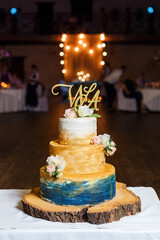 Elegant wedding cake in gold and blue colors decorated with fresh flowers and gold topper, standing...