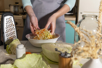 Sauerkraut canning. A young woman prepares homemade sauerkraut with carrots in the kitchen. Fermented food.