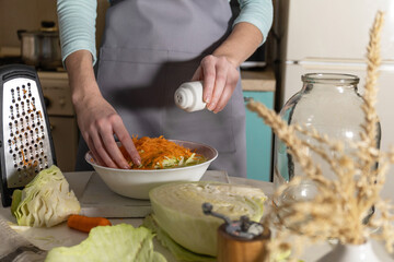 Sauerkraut canning. A young woman prepares homemade sauerkraut with carrots in the kitchen. Fermented food.