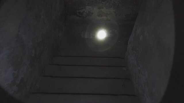A man goes down the stairs into an old dark basement shining a flashlight. Point of view. Low key