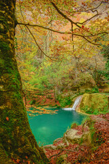 A waterfall of turquoise water with trees around it on an autumn day