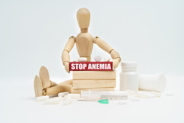 A figurine of a man sitting among pills lifts a red wooden block with an inscription STOP ANEMIA...