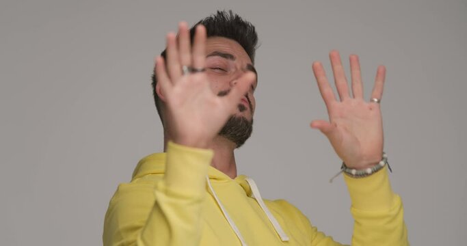 unshaved casual guy in yellow sweatshirt having fun, making hand gesture, playing salt bae role and sprinkling salt while having fun on grey background