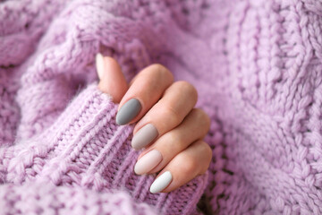Women's hands with a beautiful matte oval manicure in a warm purple knitted sweater. Winter trend,...