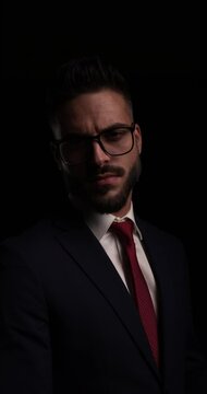 attractive elegant guy in suit wearing eyeglasses looking to side, pointing fingers in the air and confidently smiling on black background