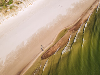 Couple walking on the sandy beach from above. Shadows and the sea waves. Bird view.