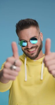 handsome casual man wearing sunglasses, smiling and giving a thumbs up with both hands