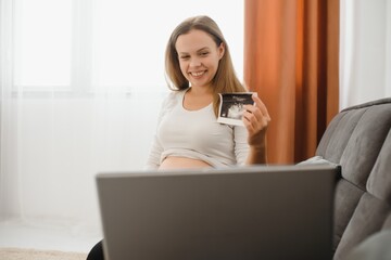 selective focus of cheerful pregnant woman showing ultrasound photos while having video call