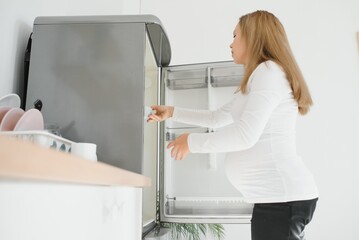 pregnant woman at home in the kitchen opens the refrigerator