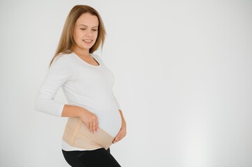 Close up of pregnant woman putting on a bandage at gray background with copy space. Orthopedic abdominal support belt concept.