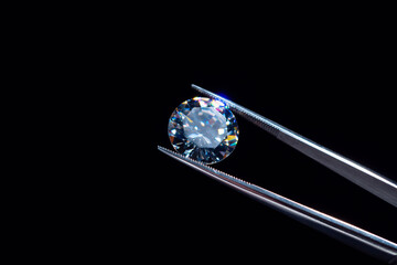 Diamond selective focus held in metal jeweller tweezers, brilliant stone cut inspection of polish quality and contamination. Natural carbon material, for industrial and fashion applications.