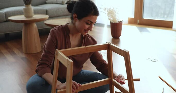 Excited millennial lady mounting carry home furniture spinning screws in wooden details using hex key tool. Smart young Indian woman enjoy furnishing apartment assemble wooden decorative shelf herself