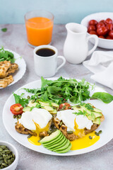 Healthy breakfast. Poached eggs on toast with avocado pieces, arugula, mizuna and chard leaves and cherry tomatoes on a plate on a served table. Flexetarian diet. Vertical view