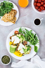 Healthy lunch. Toast with poached eggs, avocado pieces, arugula, mizuna and chard leaves and cherry tomatoes on a plate on a served table. Flexetarian diet. Top and vertical view. Copy space