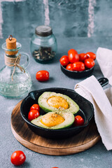 Raw avocado halves, ready to bake, stuffed with egg and cherry tomatoes in a pan on the table. Healthy eating. Flexitarian diet. Vertical view