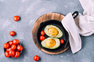 Raw avocado halves, ready to bake, stuffed with egg and cherry tomatoes in a pan on the table. Healthy eating. Flexitarian diet. Top view. Copy space