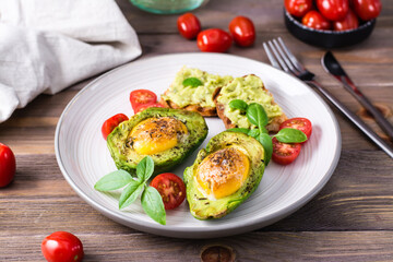 Ready-to-eat appetizer baked avocado with egg, toast and cherry tomatoes on a plate on a wooden table. Healthy eating. Flexitarian diet