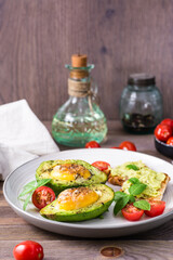 Hot appetizer baked avocado with egg, toast, cherry tomatoes and basil on a plate on a wooden table. Healthy eating. Flexitarian diet. Vertical view