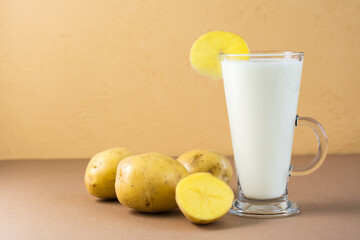 Alternative vegan vegetable potato milk in a glass and potato tubers next on a brown background. Vegetarian and flexitarian food.
