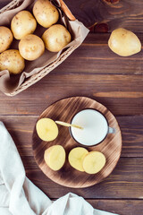 Alternative vegetable vegan potato milk in a glass and potato tubers side by side on a wooden table. Vegetarian food. Vertical and top view