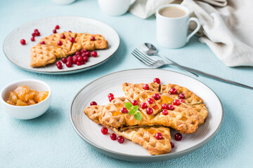 Crispy croffles with red currants, honey and mint on plates, a cup of coffee and jam on a light table. Sweet delicious breakfast