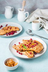 Crispy croffles with red currants, honey and mint on plates, a cup of coffee and jam on a light table. Sweet delicious breakfast. Vertical view