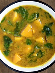 Close-up soup from butternut squash and spinach leaves in enamel bowl view. Top view comfort food.