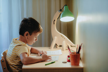 Boy doing his homework while sitting by desk.