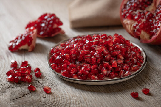 red ripe juicy peeled pomegranate seeds close-up in a plate and sprinkled on a wooden table, rustic style