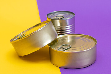 A Group of Stacked Tin Cans with Blank Edges on Split Yellow and Violet Background. Canned Food. Different Aluminum Cans for Safe and Long Term Storage of Food. Steel Sealed Food Storage Containers