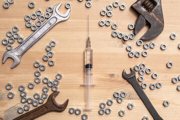 Syringe with a medicine lies on a wooden table among a variety of wrenches and metal nuts. Vaccine production concept. Top view. 