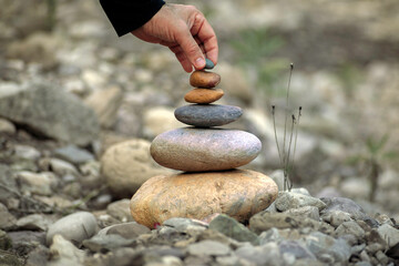 Zen-style stone pyramid in a natural setting with a hand that gently places a stone on top, which...