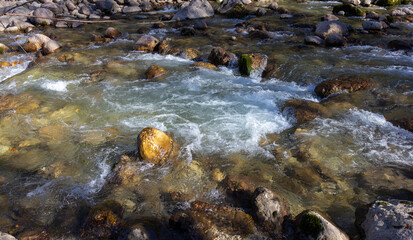 Autumn morning on a mountain river, a shallow riverbed with clear water and the rays of the sun illuminating the rocky bottom.