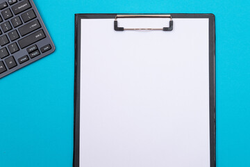 Black Clipboard with Blank White Sheet of Paper Lying on Blue Table - Top View, Flat Lay