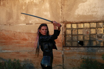 Young woman with katana sword near old wall