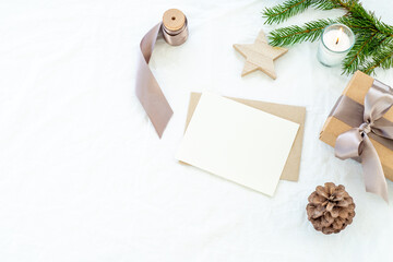 Christmas decorations composition.Christmas blank greeting card mockup scene.Gift Christmas box, fir branch, pine cone, wooden star and lighted candle.White linen background top view, flat lay
