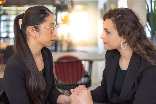 Dos mujeres de negocios, asi&aacute;tica y cauc&aacute;sica, se miran cogidas de las manos