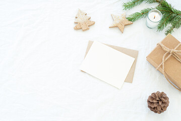Christmas decorations composition.Decorative corner.Christmas blank greeting card mockup scene.Gift Christmas box, fir branch, pine cone, wooden shapes and lighted candle.White linen background 