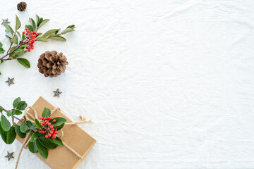 Christmas decorations composition on white linen background with gift box, pine branches, pine cone, wooden stars and red berry branches. Greeting card mockup.Banner. Copy space, top view, flat lay