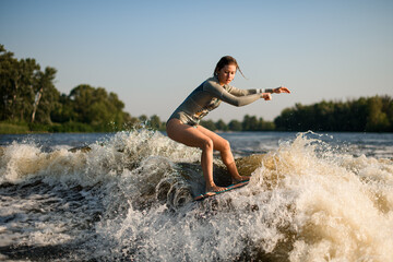 Fototapeta premium active flexible woman skillfully balancing on great splashing wave on wakesurf board.